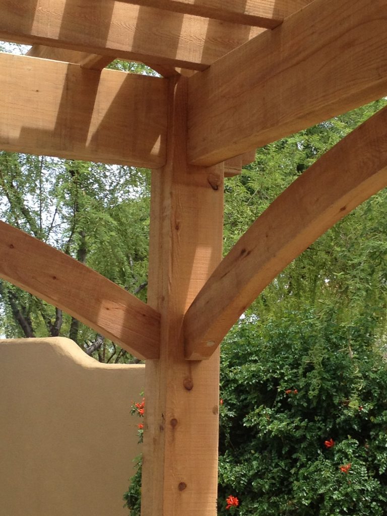 Close view of a natural cedar post, arched knee brace, and Roosevelt beam end on a poolside timber pergola