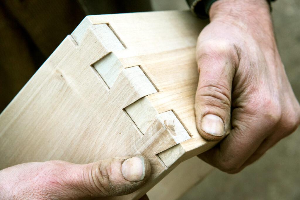 Hands holding two interlocking dovetailed wood pieces, demonstrating how The Dovetail Difference® joinery fits together.