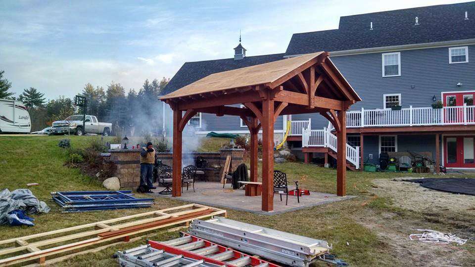 Completed 16x20 Douglas Fir timber pavilion with a gable roof installed beside a backyard patio and fire pit in New Hampshire by Western Timber Frame.