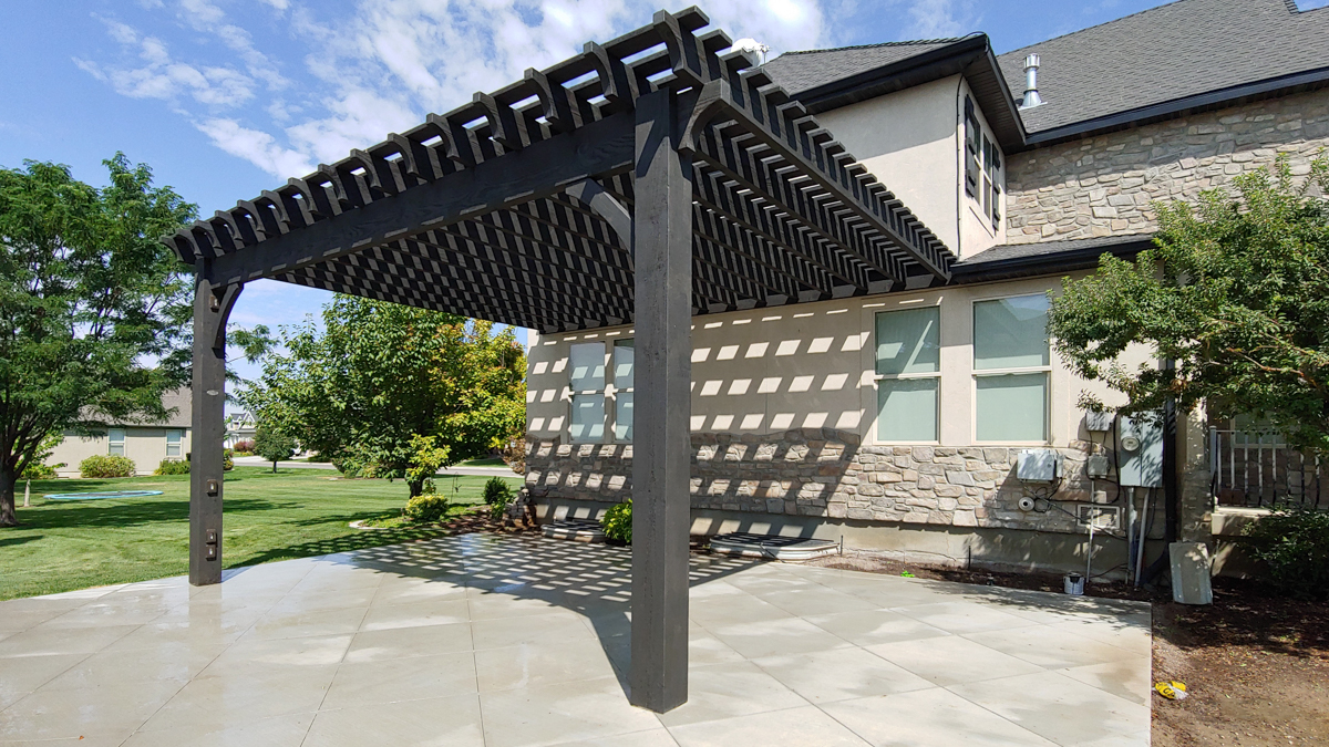 Freestanding dark-stained heavy timber pergola with dense shade rafters over a backyard patio