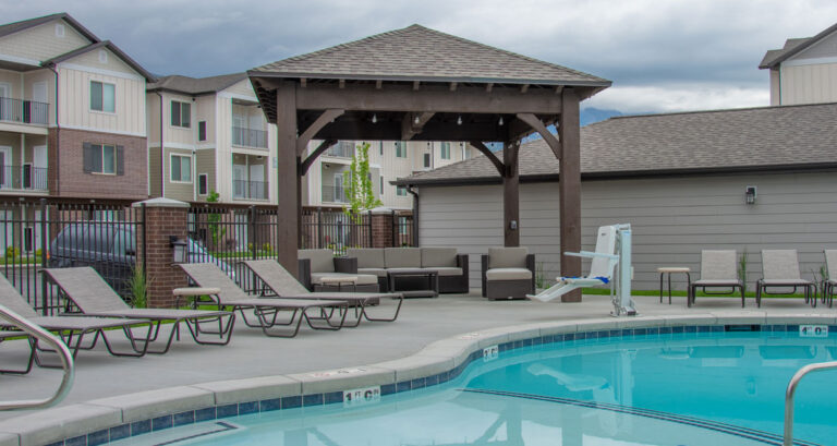 Hipped roof heavy timber pavilion with exposed beams providing shaded lounge seating by poolside.”