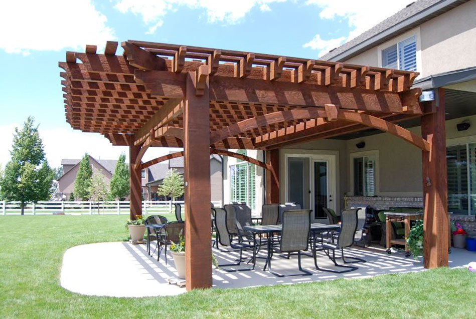 Angled view of a Rich Sequoia-stained timber pergola with arched beams and grid-style shade roof over a backyard dining patio.