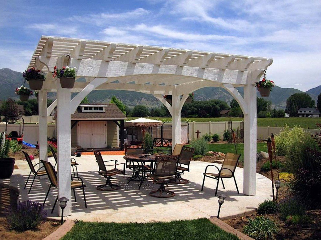 Alpine-stained timber pergola with arched support beams over a patio dining area, surrounded by flowers and mountain views.