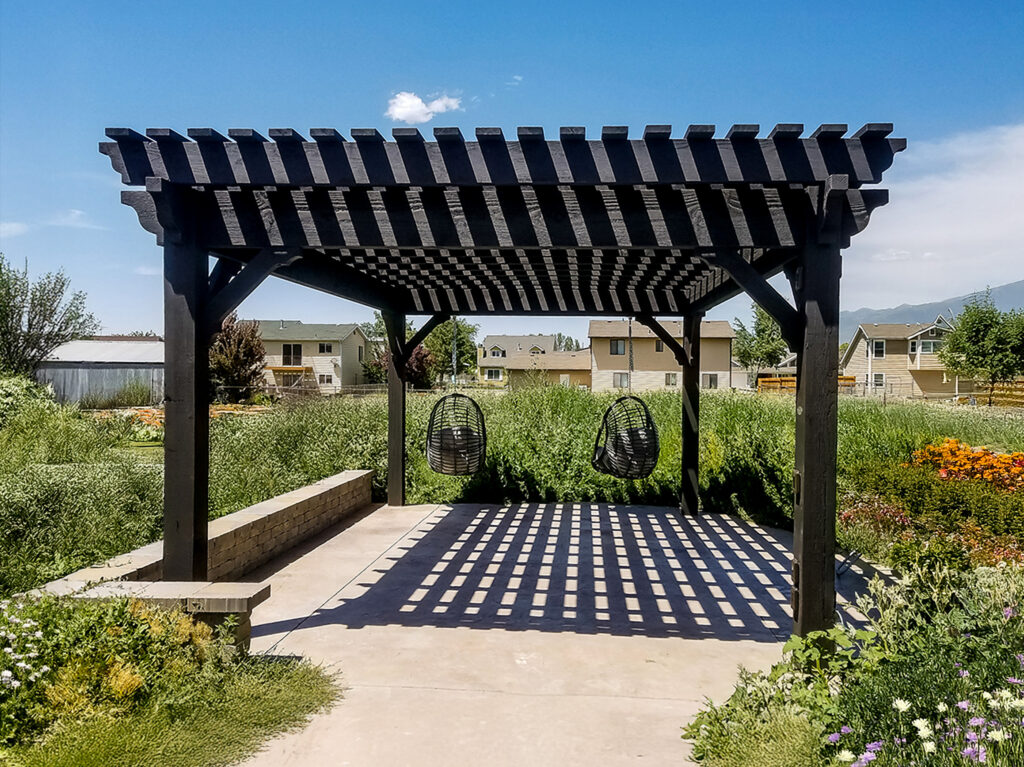 Black timber pergola with hanging swing chairs and deep shade grid over concrete patio