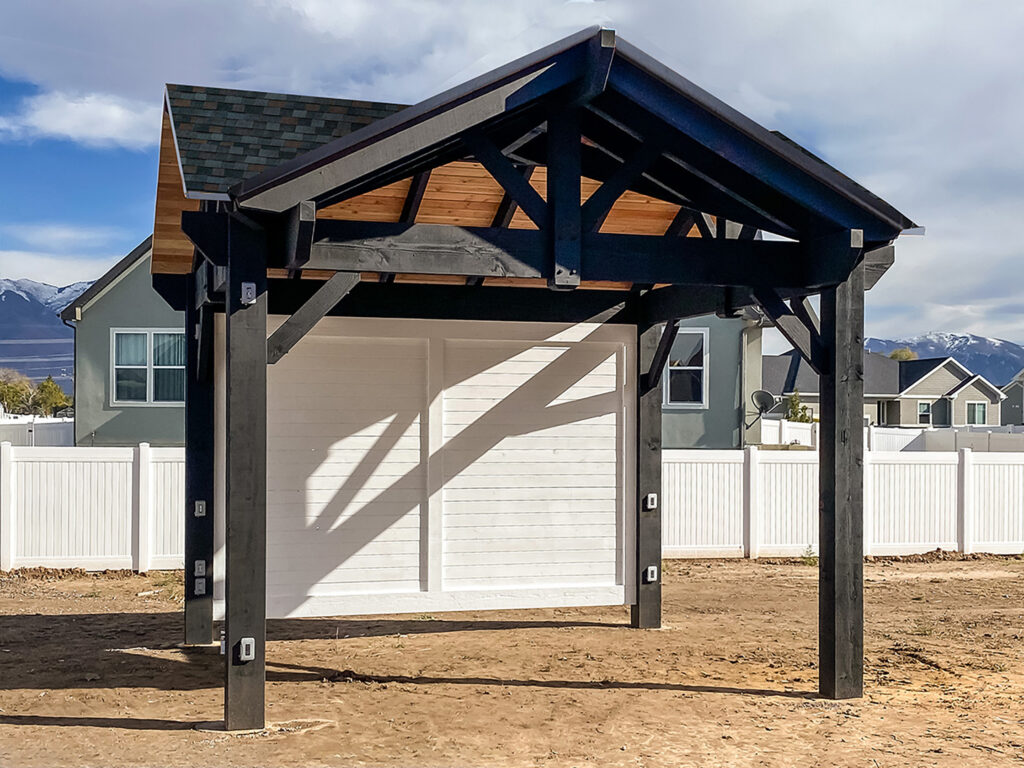 Black timber pavilion with gable roof, white privacy panel, and TimberVolt power posts in residential backyard