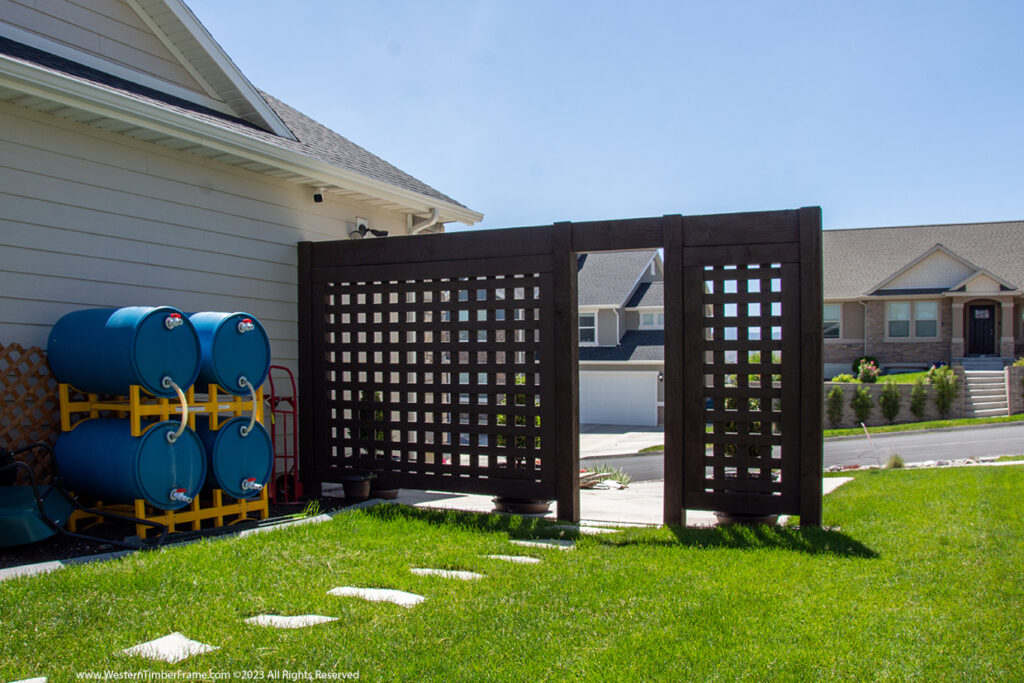 Western Timber Frame™ timber frame privacy wall with a latticed design, partially concealing utility barrels next to a home, creating a clean and attractive boundary.