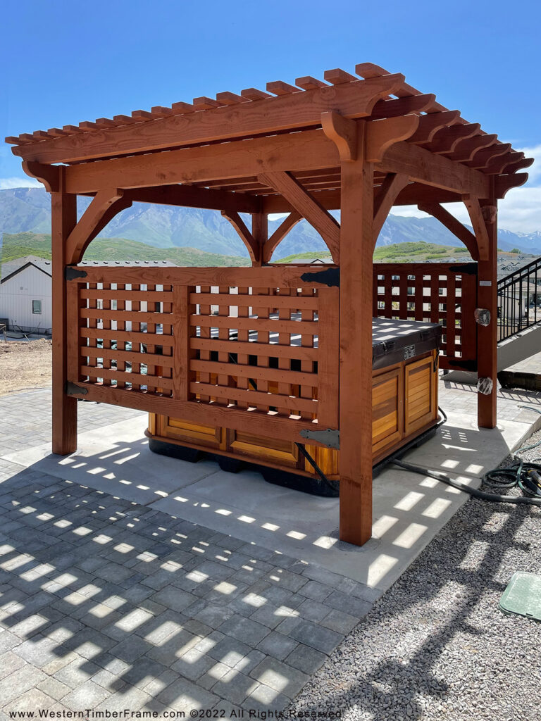 Timber frame pergola with rich stain and TimberClad® metal accents sheltering a hot tub, creating a cozy, spa-like outdoor oasis with mountain views.