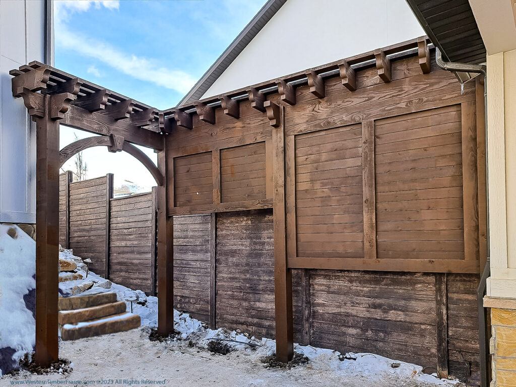 Western Timber Frame™ timber frame privacy trellis and entry structure with dark stain, featuring heavy timber beams, solid privacy panels, and an arched timber brace.