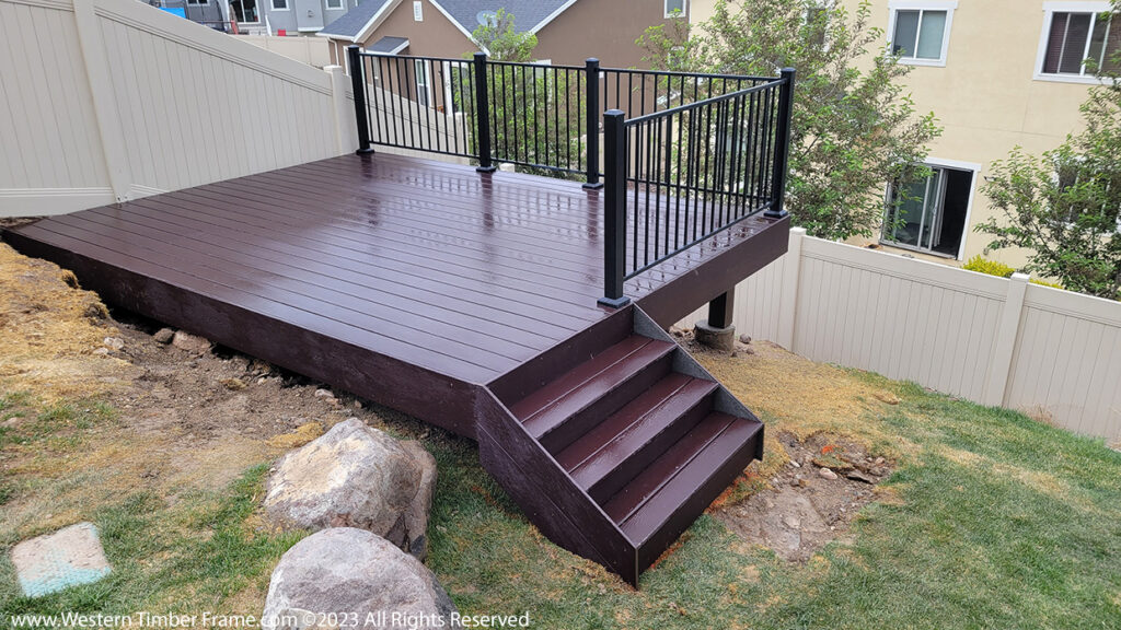 Western Timber Frame™ timber frame deck with dark stain and black metal railing, built into a steeply sloped backyard to create a level, functional outdoor living space.