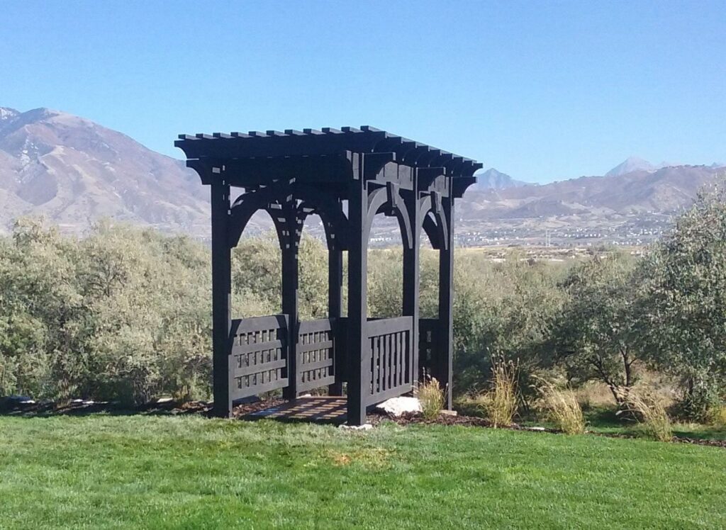 Western Timber Frame™ timber frame arbor with a dark stain, featuring solid privacy panels and arched knee braces, set against a backdrop of open landscape and distant mountains.
