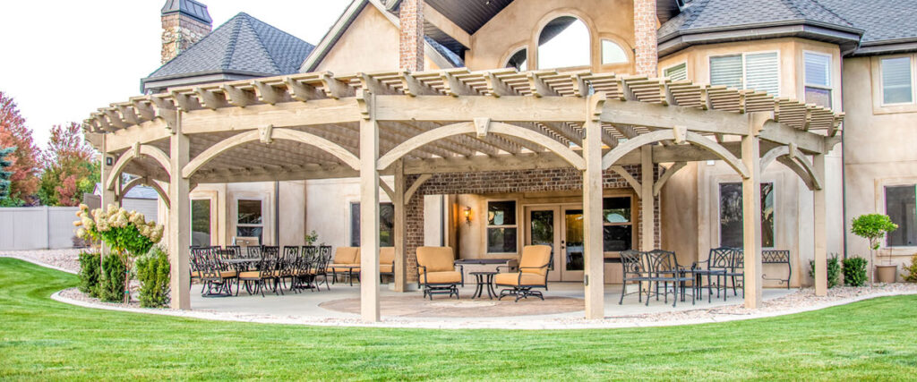 Western Timber Frame™ timber frame pergola with a gracefully curved design, integrated TimberVolt® power posts, and spacious outdoor seating and dining areas in a landscaped backyard.