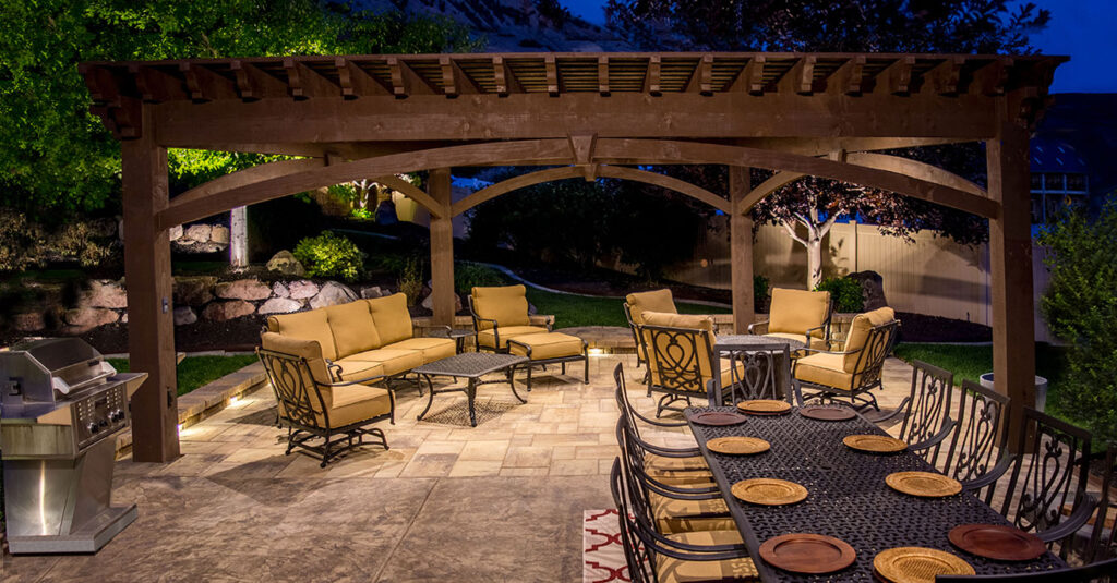 Western Timber Frame™ timber frame pergola tailored to fit the landscape, featuring a TimberVolt® power post, elegant outdoor seating, and a large dining table set under soft evening lighting.
