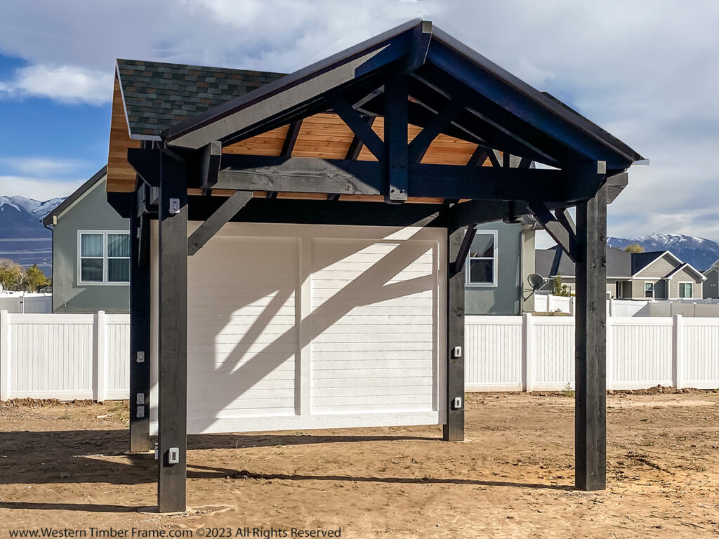 Western Timber Frame™ timber frame pavilion featuring a dark-stained structure with a tongue and groove privacy wall, set in a backyard with mountain views.