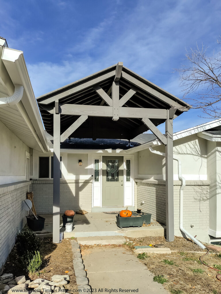 Western Timber Frame™ timber frame pavilion porch cover with a gabled roof design, finished in a gray stain to complement a white painted brick home.