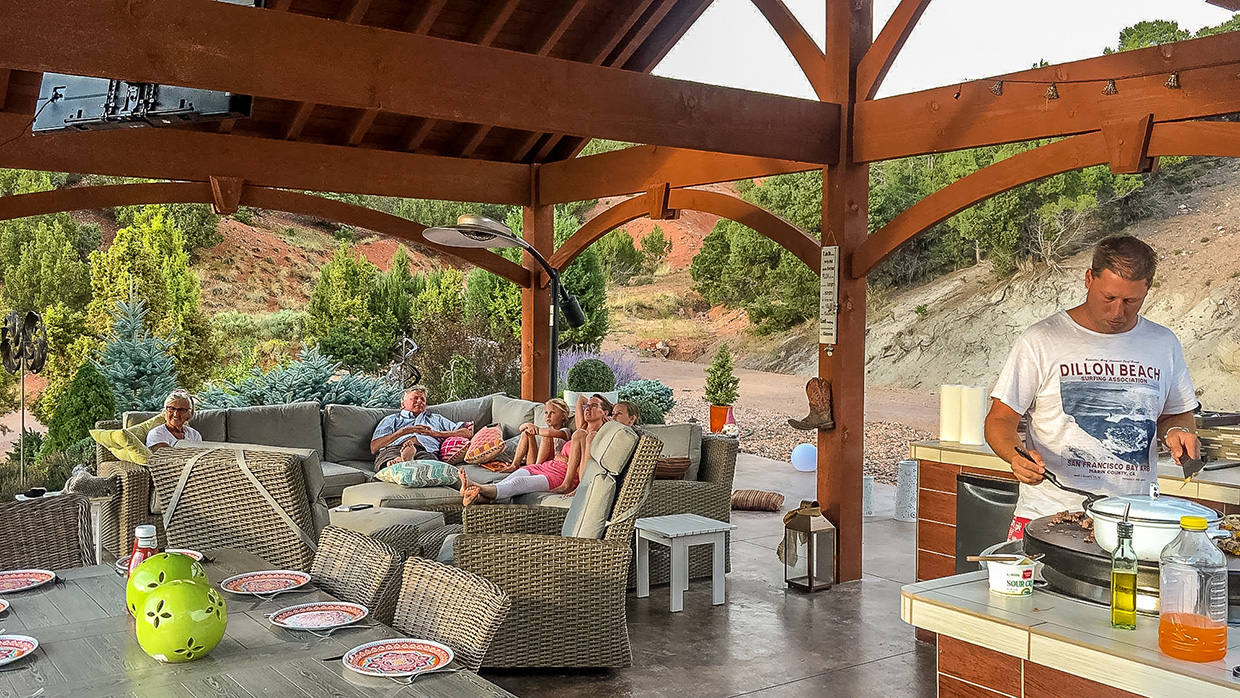 Open-air timber frame outdoor living space featuring a spacious pergola, comfortable lounge seating, and lush garden surroundings