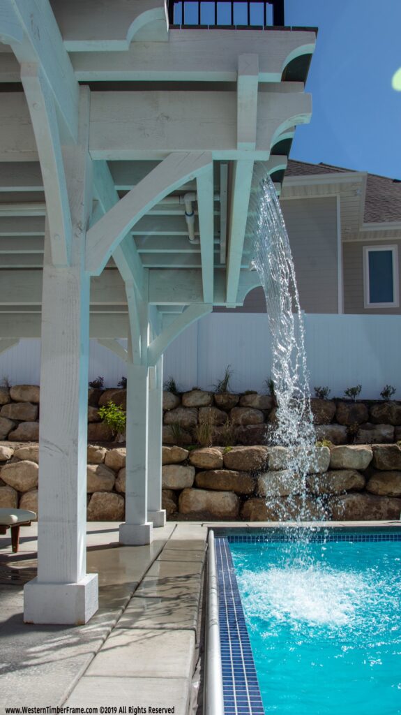 White two-story Western Timber Frame pergola with mezzanine-level diving deck, waterfall feature, and timber frame roof design.