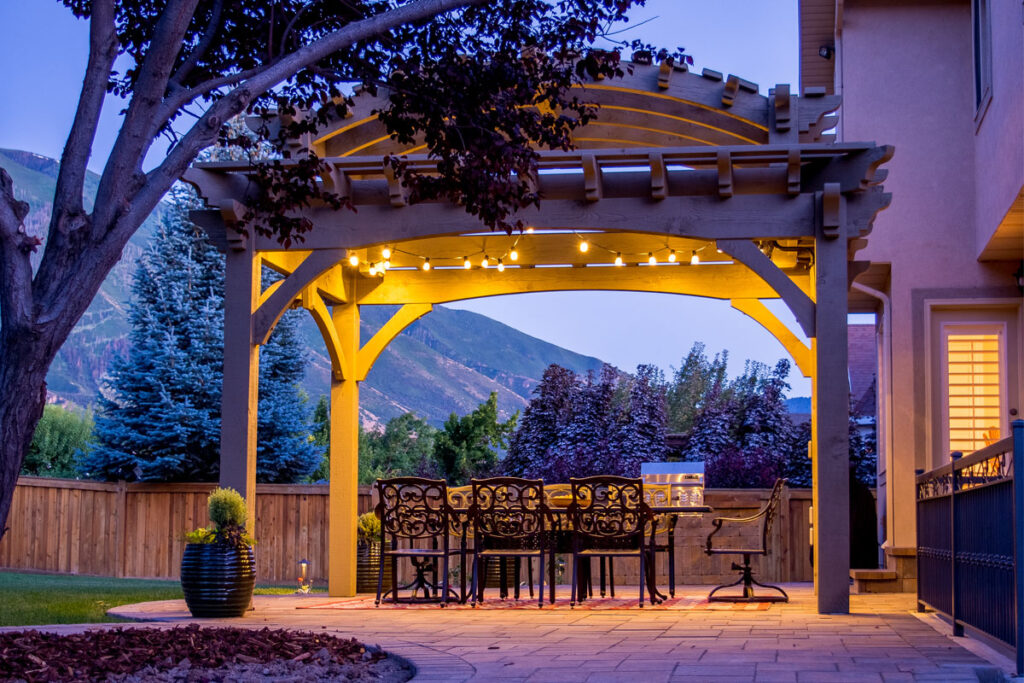 Tiered barrel roof timber pergola with TimberVolt® power, glowing evening lights, and dining table beneath by Western Timber Frame