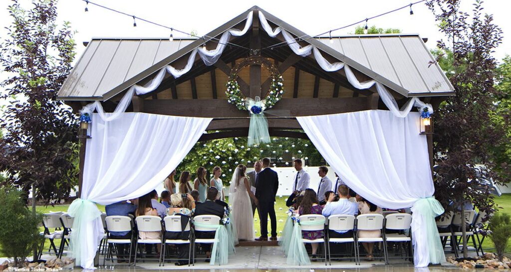 Timber frame 3-gable poolside pavilion with wedding decor, integrated power, and guests gathered for a wedding by Western Timber Frame 🔤 Title Tag:
