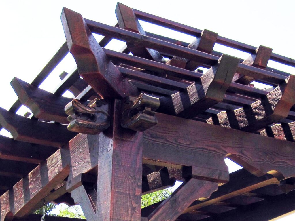 Close-up of a carved wood dragon head on the corner of an Asian-style timber frame pergola by Western