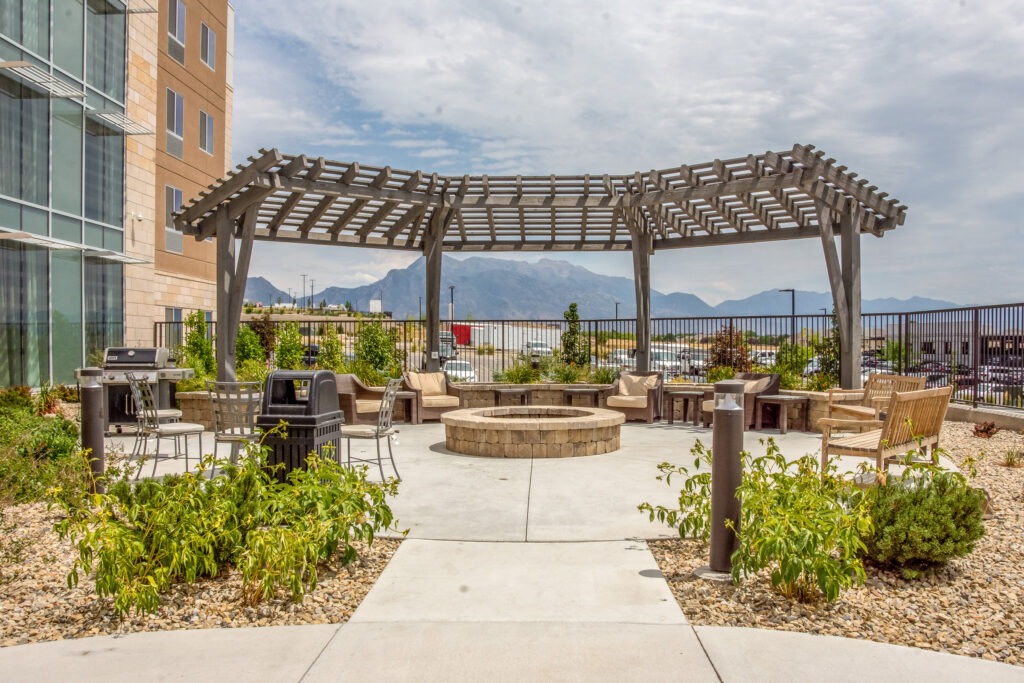 Curved timber trellis stained in Canyon Grey at a Staybridge Suites hotel patio with fire pit, mountain views, and lounge seating.