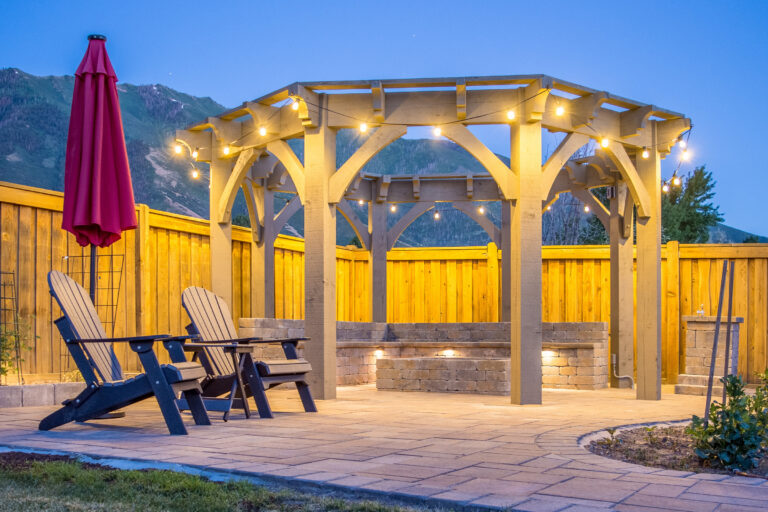 Arched timber frame pergola with integrated lighting over a backyard patio at dusk.