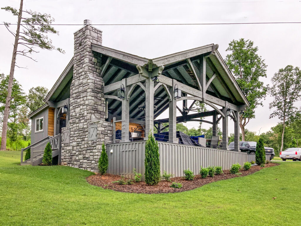 Timber frame pavilion stained in Canyon Grey, attached to a home with a stone fireplace, cable railing, and covered outdoor seating area.