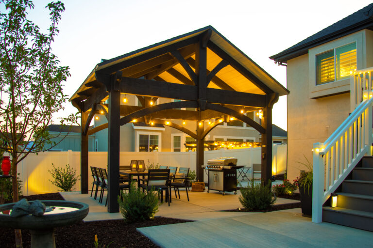 Black timber pavilion with American flag, outdoor dining table, and string lights in a backyard patio setting.