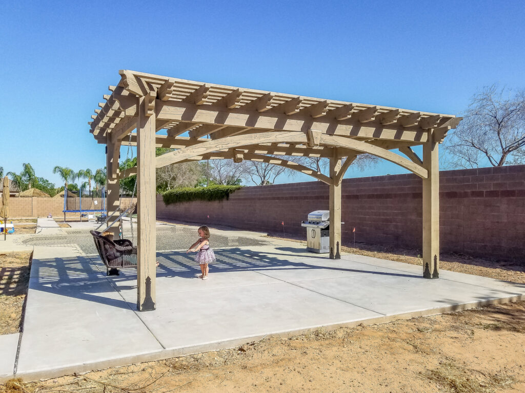 Beach Sand-stained arched beam pergola over concrete slab with hanging chair and child playing