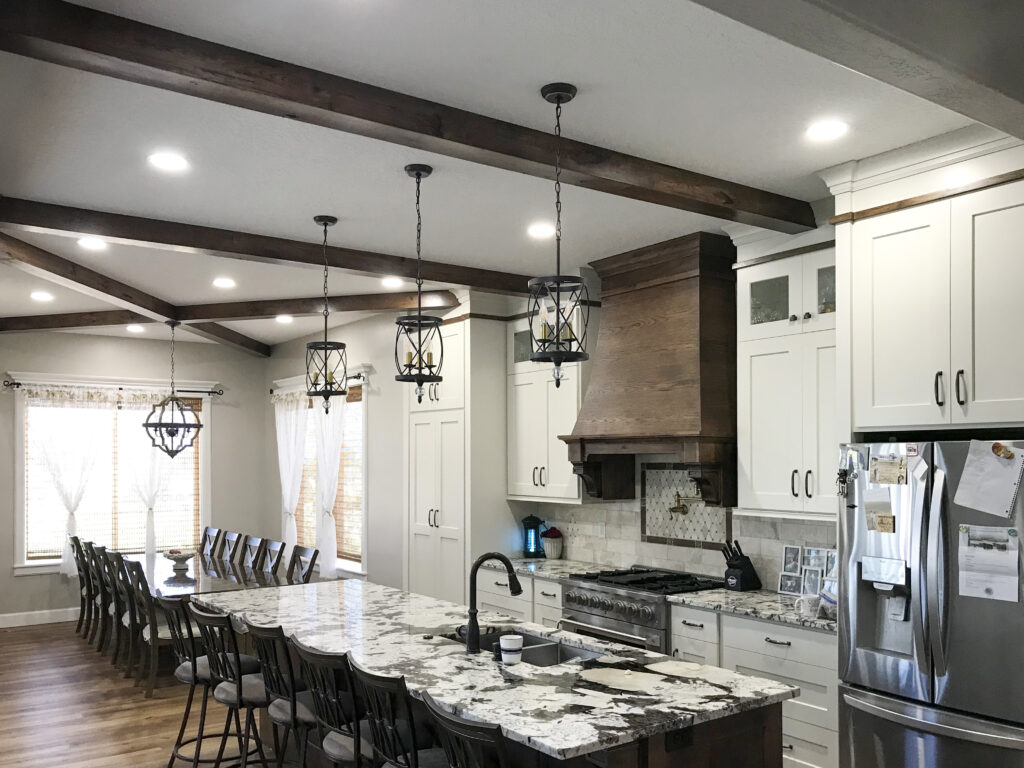 Exposed timber ceiling beams by Western Timber Frame™ accenting a luxury kitchen with white cabinetry, granite countertops, and pendant lighting