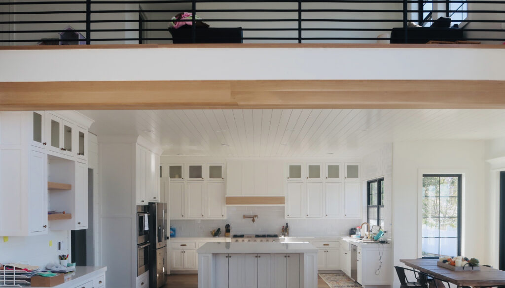 Elegant white luxury kitchen with vaulted ceiling and natural finished exposed timber beams by Western Timber Frame™, blending modern design with rustic warmth.