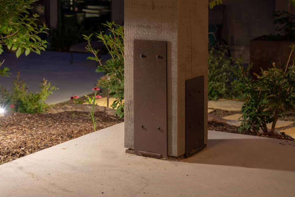 TimberClad® decorative metal accent panels on a timber frame post in a landscaped nighttime setting.