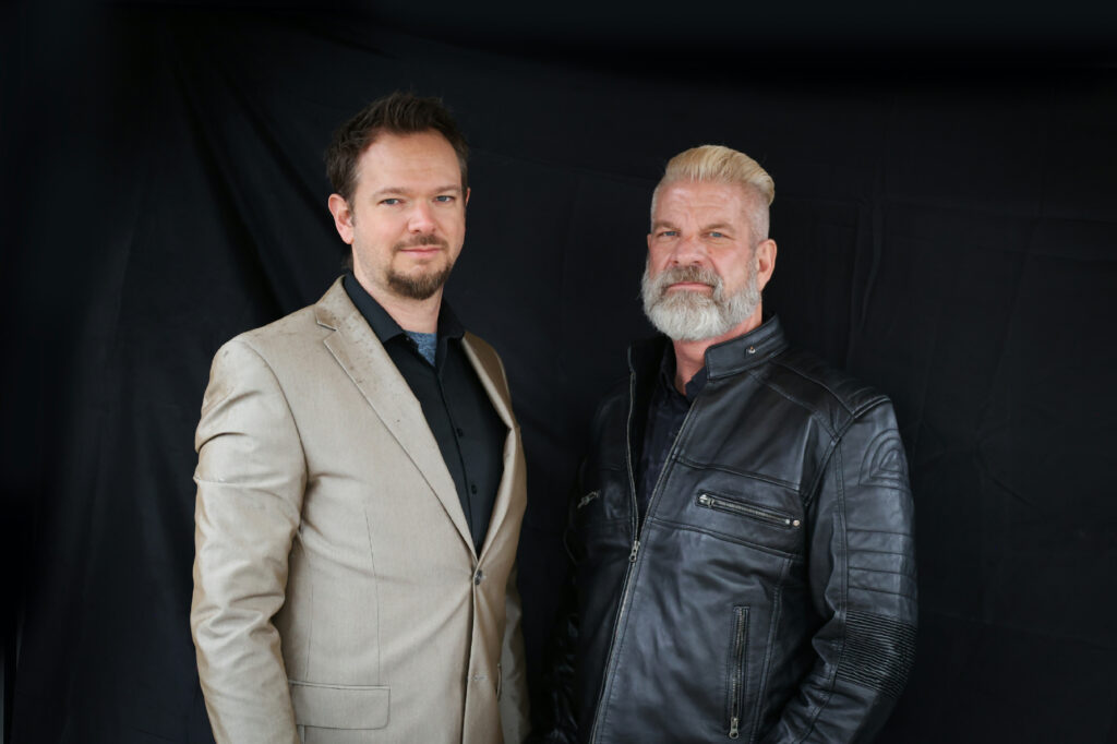 Laurence Bunker Jr. and Hyrum Thompson, co-founders of Western Timber Frame, standing together in formal attire against a black background.