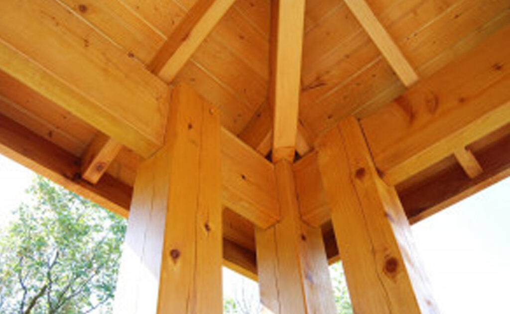 Underside view of a cedar timber pavilion roof with triple post support and exposed beam joinery.
