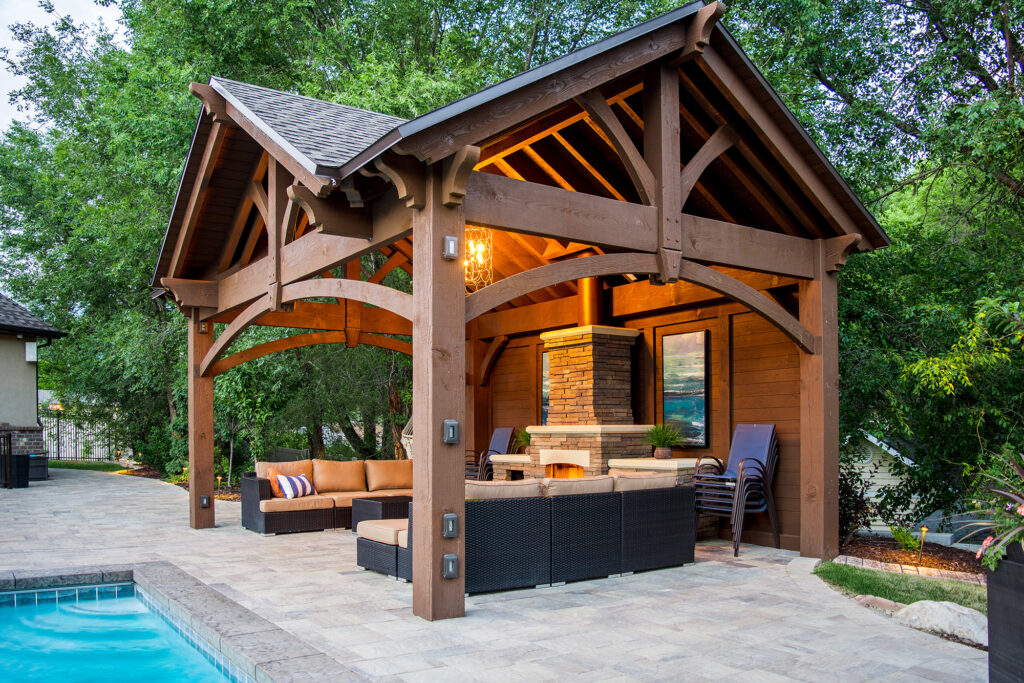 Timber frame pavilion with integrated TimberVolt power post beside pool and fireplace