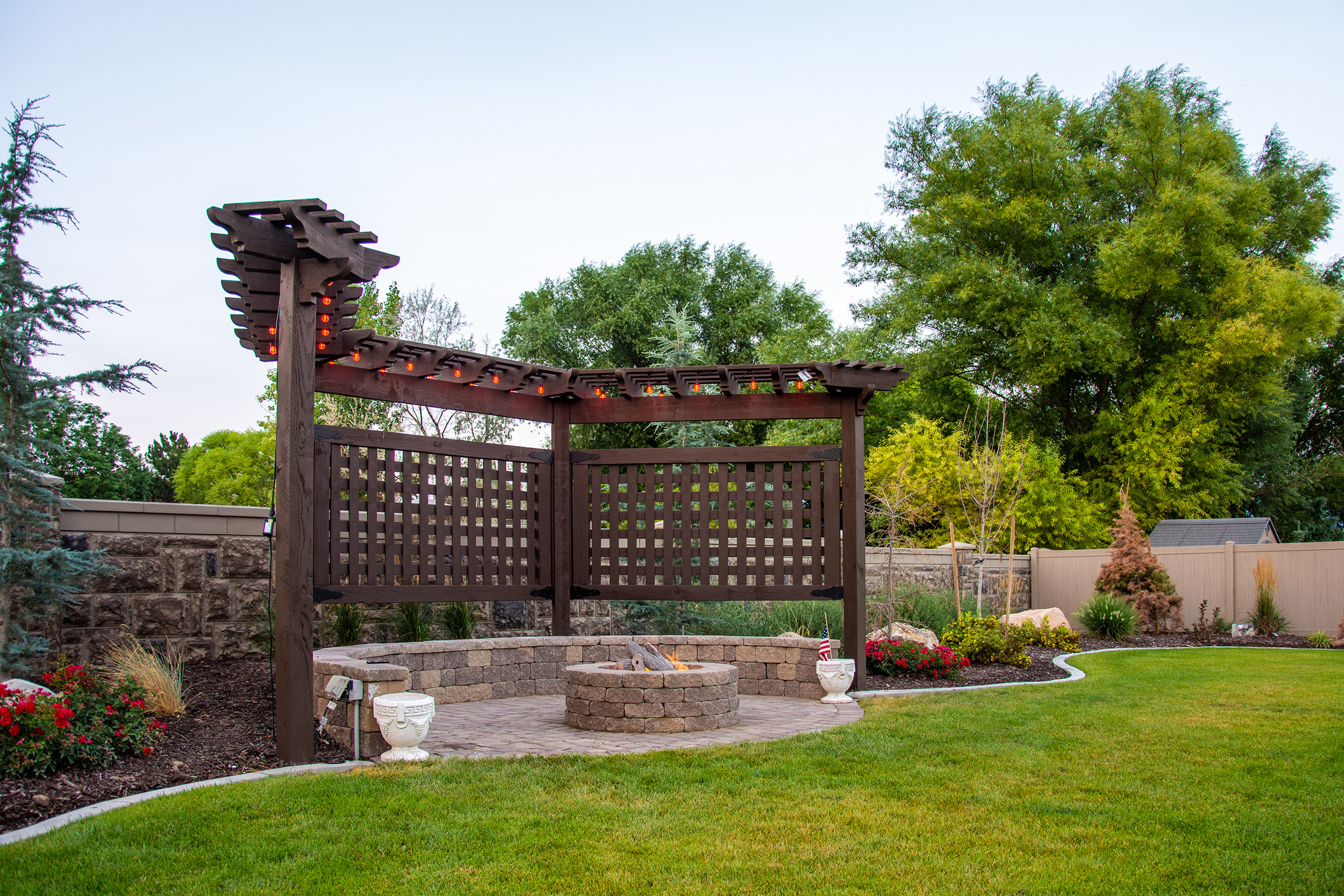 Dark timber frame trellis with string lights guiding lines and flow in garden landscape design around fire pit.