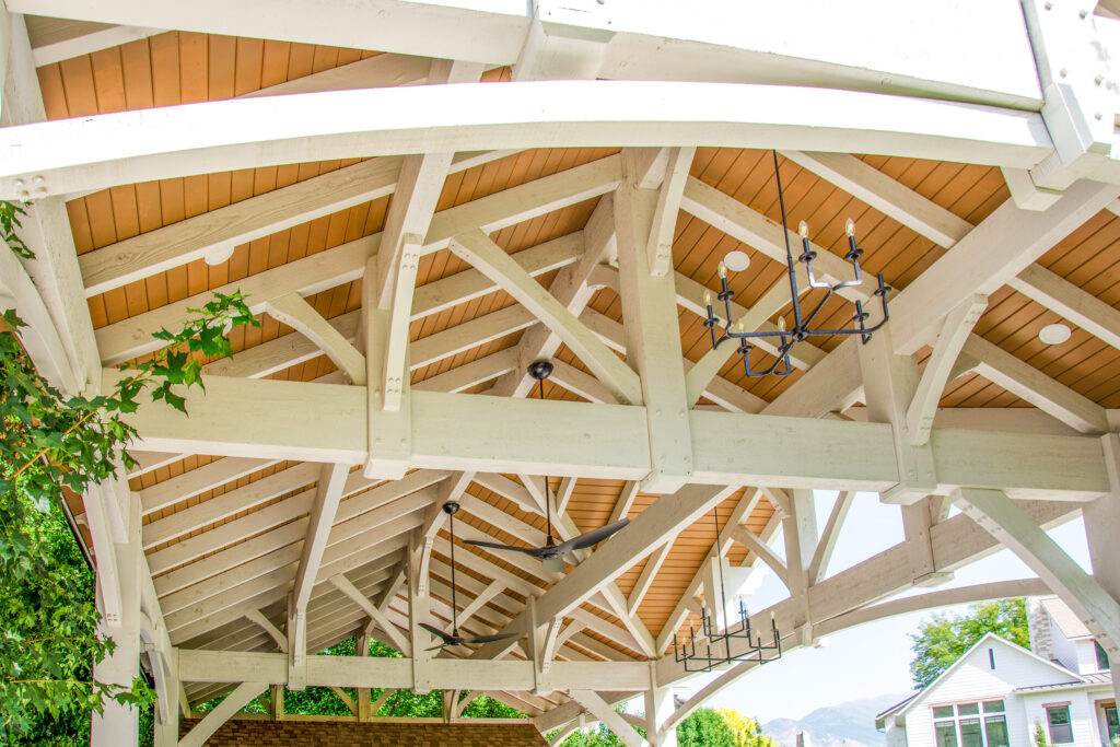 Close-up view of the timber frame roof structure of a three-gable pavilion at Maple Mountain Springs, featuring two-tone stain, decorative chandeliers, and ceiling fans.