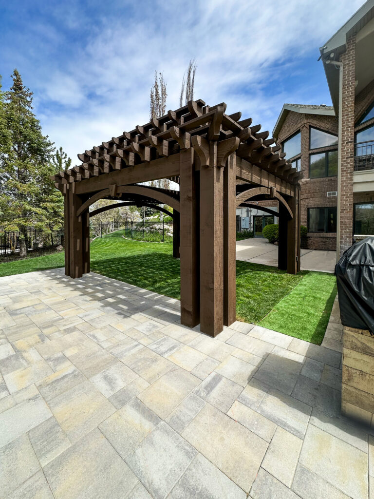 Freestanding timber pergola with triple-post corners and arched barrel roof beside a poolside patio, built from Douglas Fir with Rich Cordoba stain.