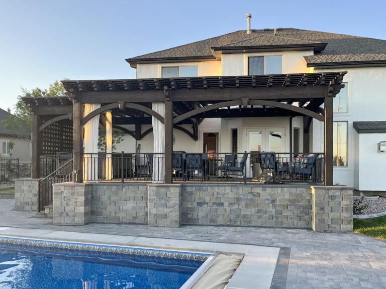 Large freestanding timber pergola with arched knee braces and lattice privacy panel beside a pool.