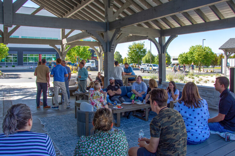 Coworkers and families relaxing and talking under a large timber frame pavilion.