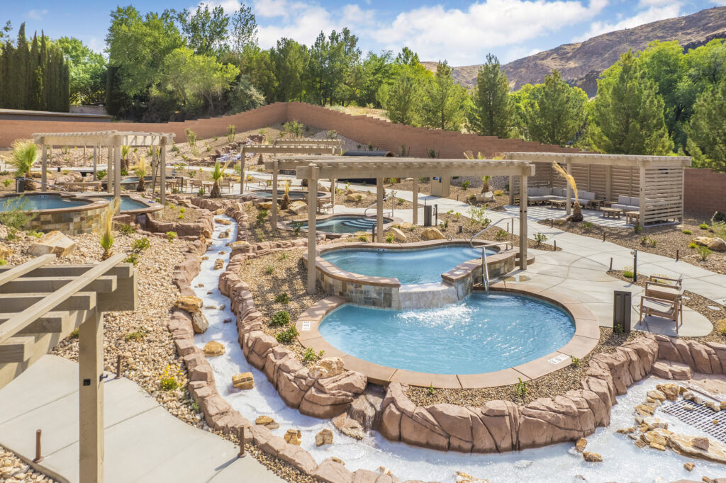 Timber frame pergolas shading mineral hot spring pools at Zion Canyon Hot Springs in Utah, surrounded by desert landscaping and flowing stream