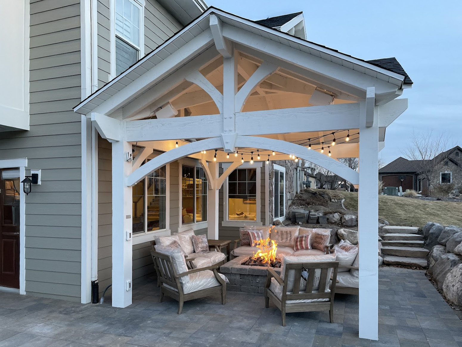 White 3-gable timber frame pavilion with outdoor fire feature and seating area on stone patio.