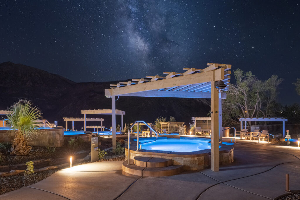 Timber frame pergola over glowing hot spring pool at Zion Canyon Hot Springs under the Milky Way night sky