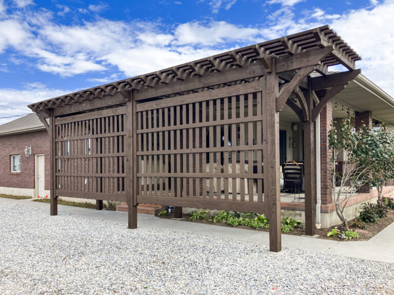 Freestanding timber frame pergola with lattice privacy panels and warm wood finish beside a brick home.