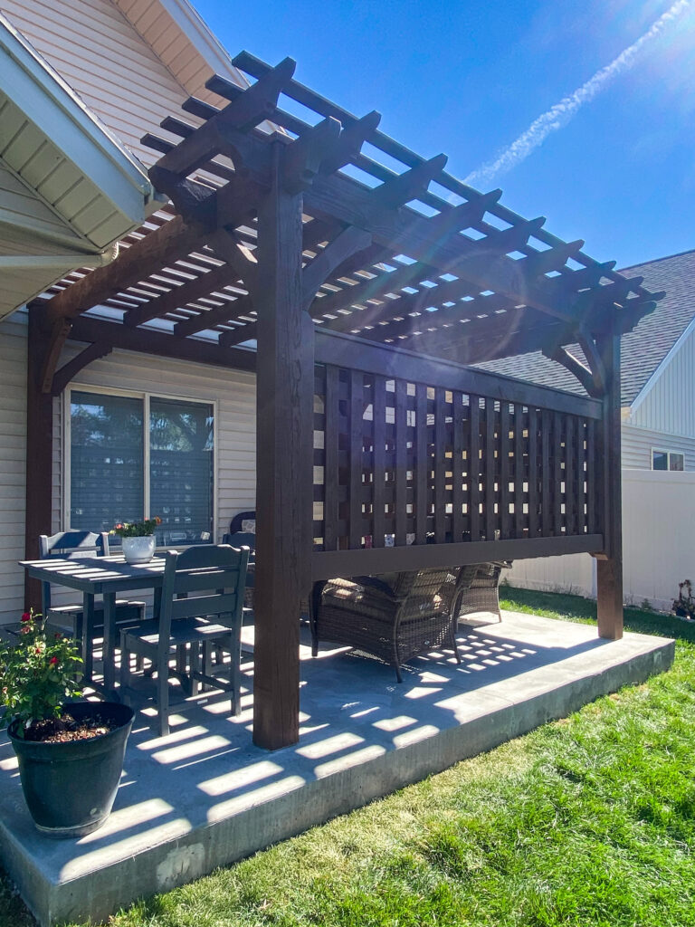 Timber pergola with lattice privacy panels shading a dining and lounge area on a backyard patio.