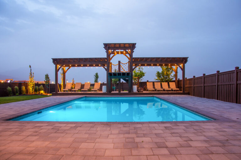 Tiered timber frame pergola with elevated timber diving deck and glowing pool at dusk