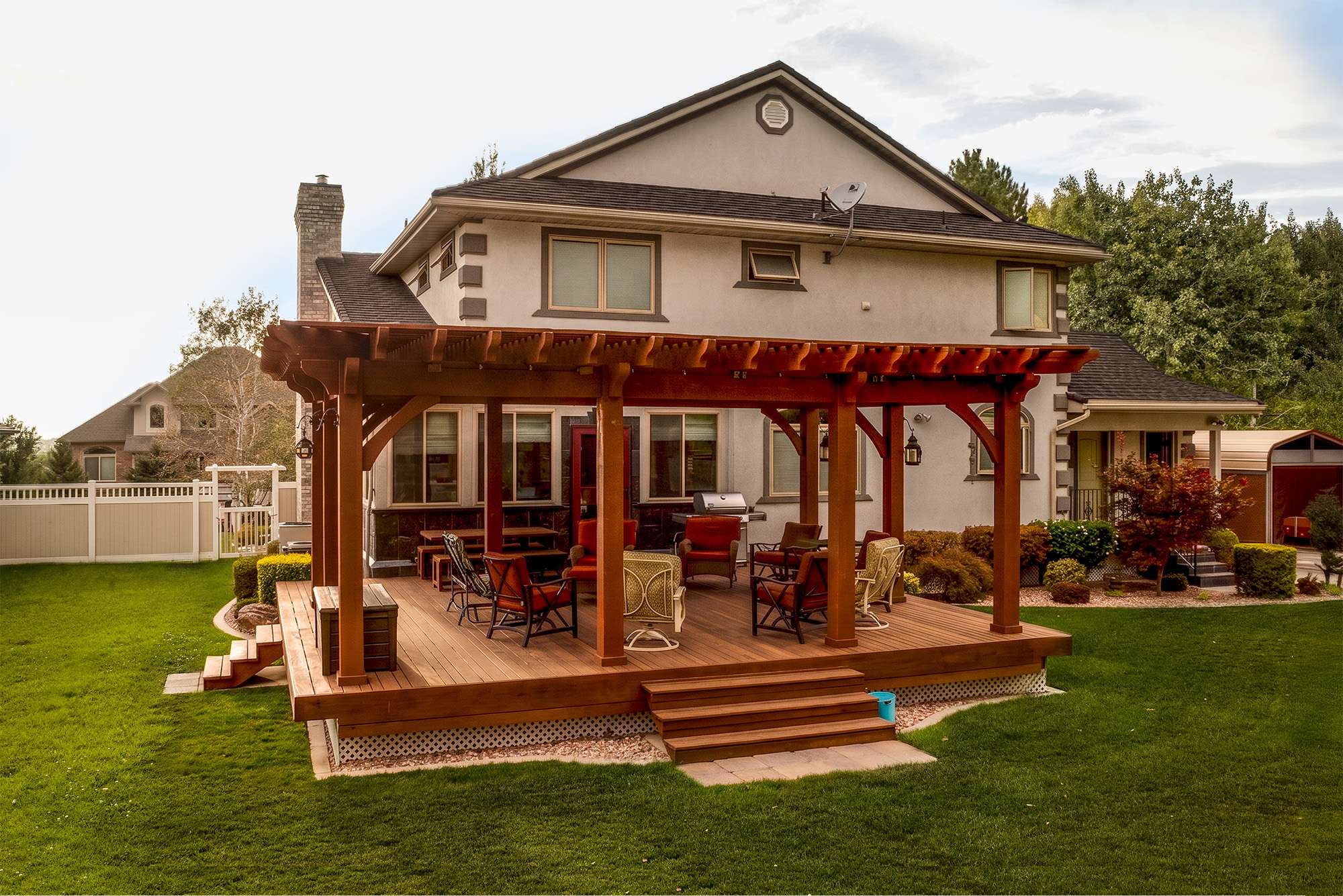 Rich Sequoia stained timber frame pergola covering a backyard deck with outdoor seating beside a large two-story home