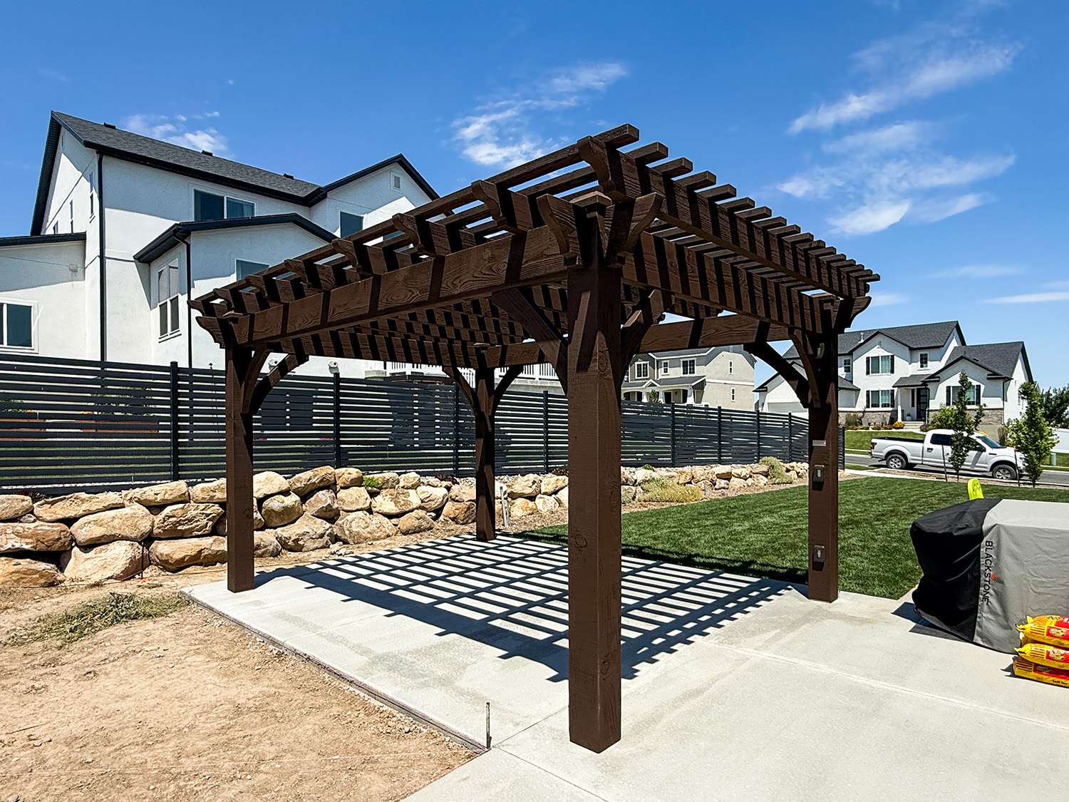 Custom heavy timber pergola with TimberVolt power posts, decorative knee braces, and closely spaced shade planks creating deep shade coverage over a backyard patio.