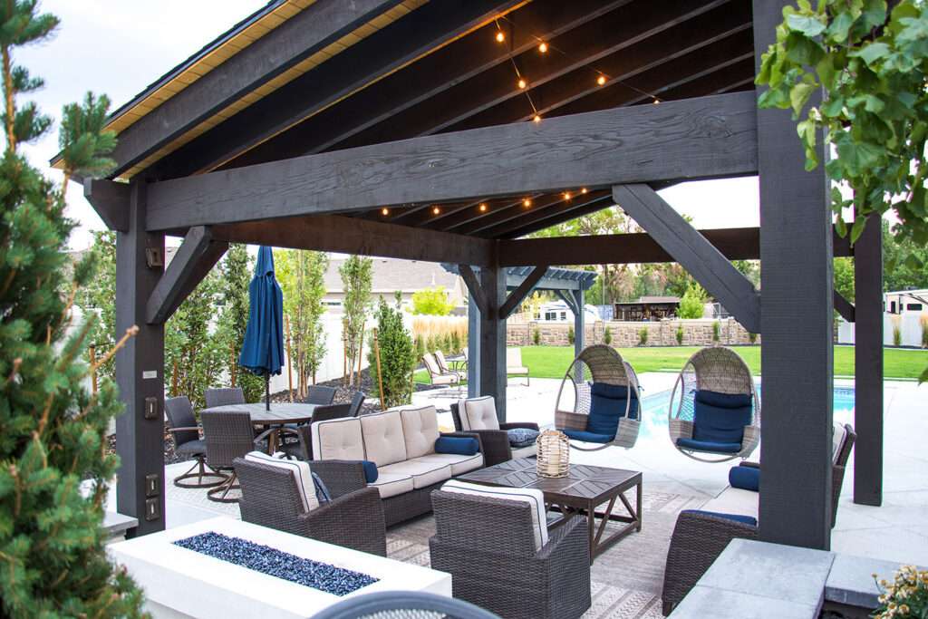 18×20 10,000 Series timber frame cabana with Rich Cordoba stain, TimberVolt® integrated outlets, poolside seating, dining area, and hanging egg chairs