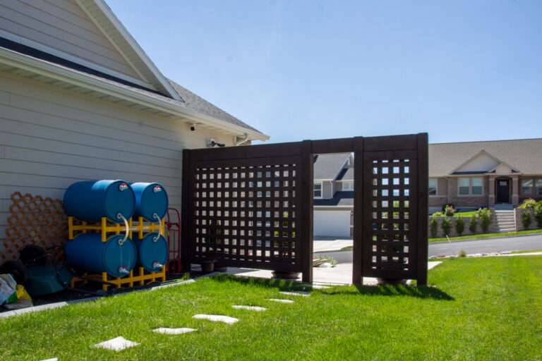 Dark-stained timber privacy trellis with lattice panels beside a residential home.