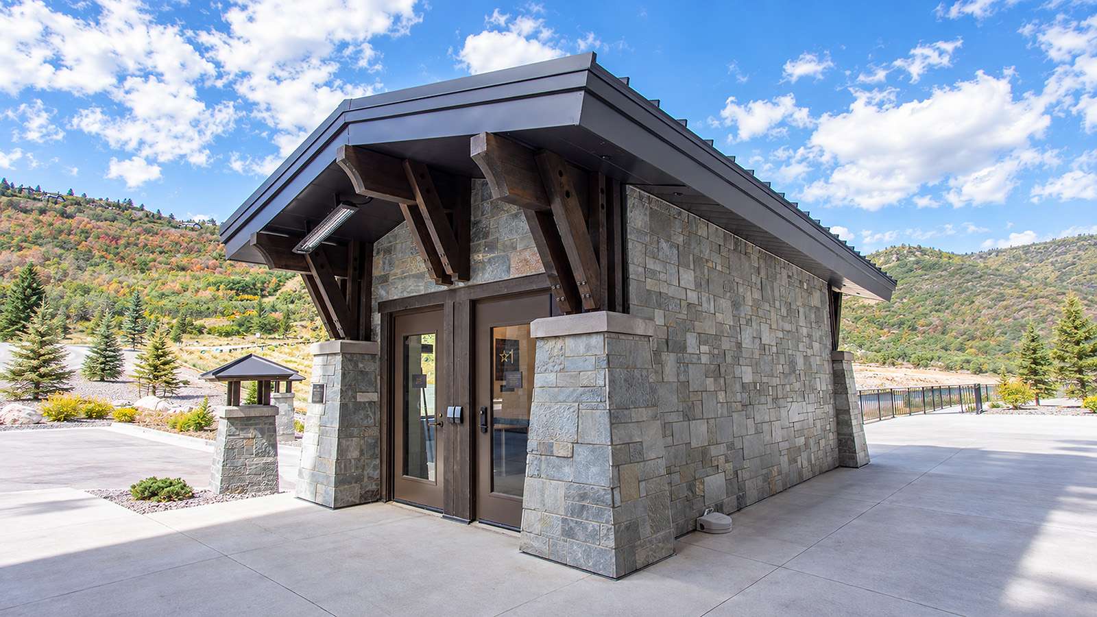 Stone entry building with heavy timber brackets supporting a deep metal roof overhang above glass doors